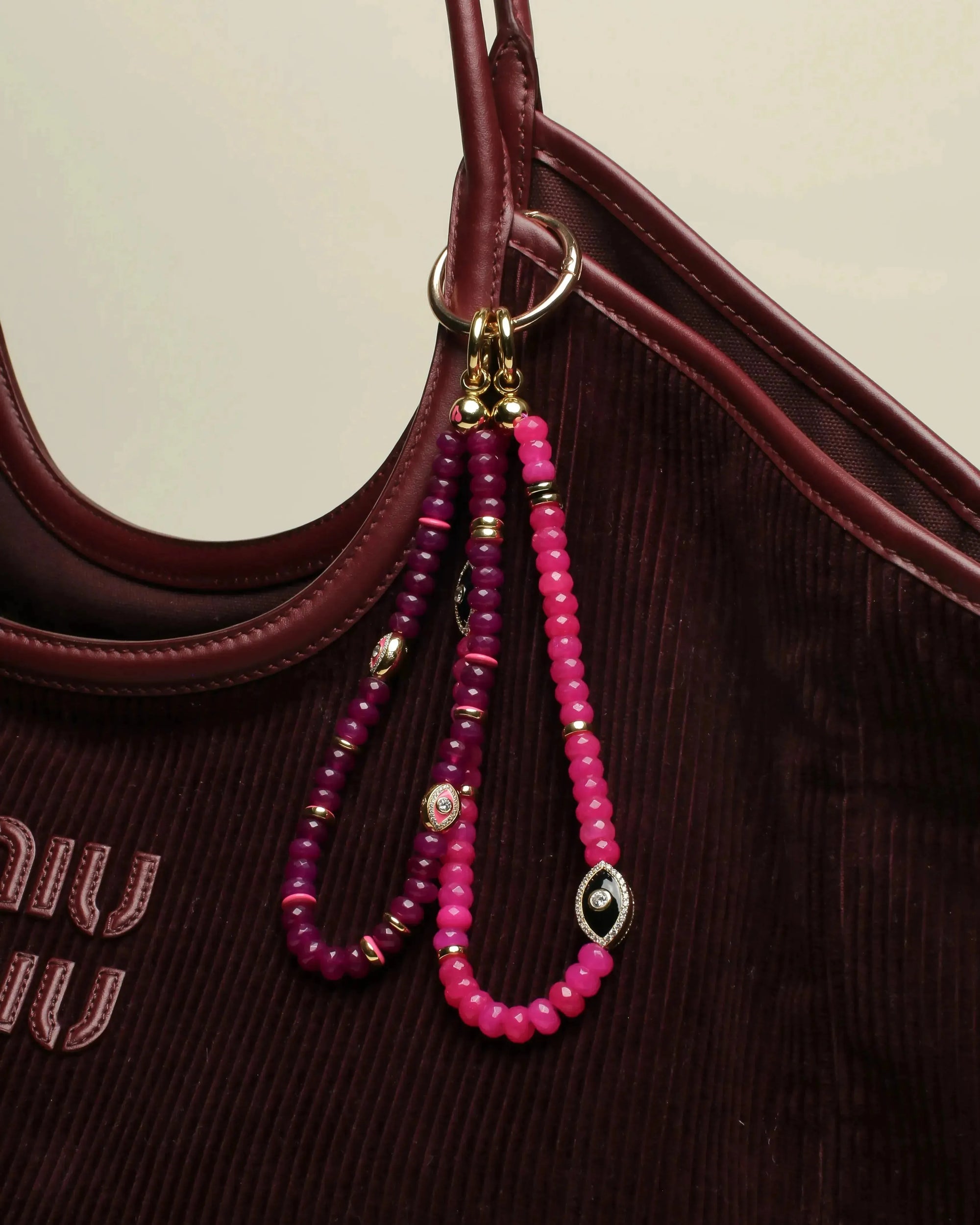 Leah Bag Charm in Amethyst &amp; Stella Bag Charm in Pink attached to a burgundy designer tote – A stylish display of two bag charms, one in faceted amethyst quartz and the other in vibrant pink quartz, clipped onto a burgundy leather designer bag, showcasing their bold yet elegant accents.