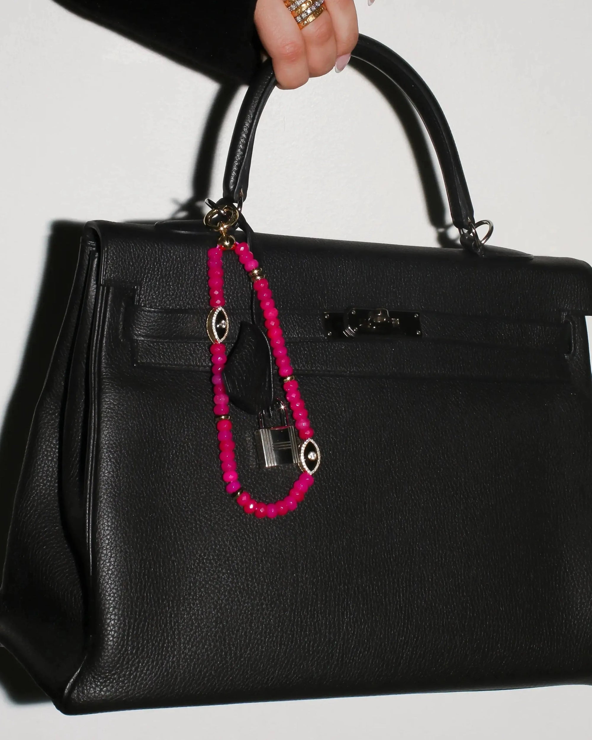 Stella Bag Charm attached to a black handbag – The pink quartz charm clipped onto a structured black handbag, adding a statement of confidence and sophistication.