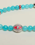 A close-up of The Leah Bag Charm in Turquoise, highlighting the intricate details of the rhodium-plated silver Evil Eye charm, pink dividers, and semi-precious turquoise quartz beads.
