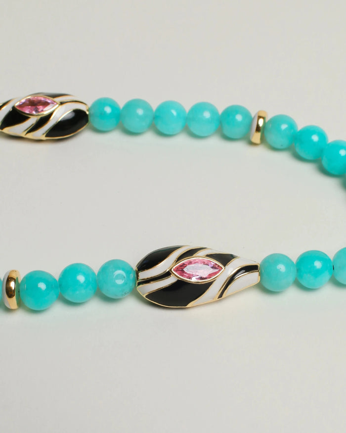  A close-up of The Minou Bag Charm in Aqua, emphasizing the intricate design of the gold-plated zebra-striped Evil Eye charm and polished dividers.