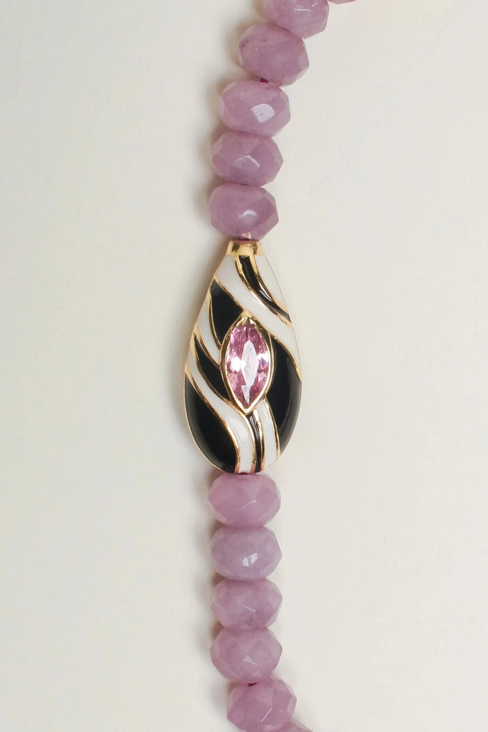  A close-up of The Minou Bag Charm in Lavender, emphasizing the intricate zebra-striped Evil Eye charm, polished gold-plated dividers, and faceted lavender quartz beads.