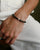 A man wearing the David Bracelet in Silver, featuring 6mm Onyx and Black Labradorite Quartz beads with a black CZ diamond evil eye charm.