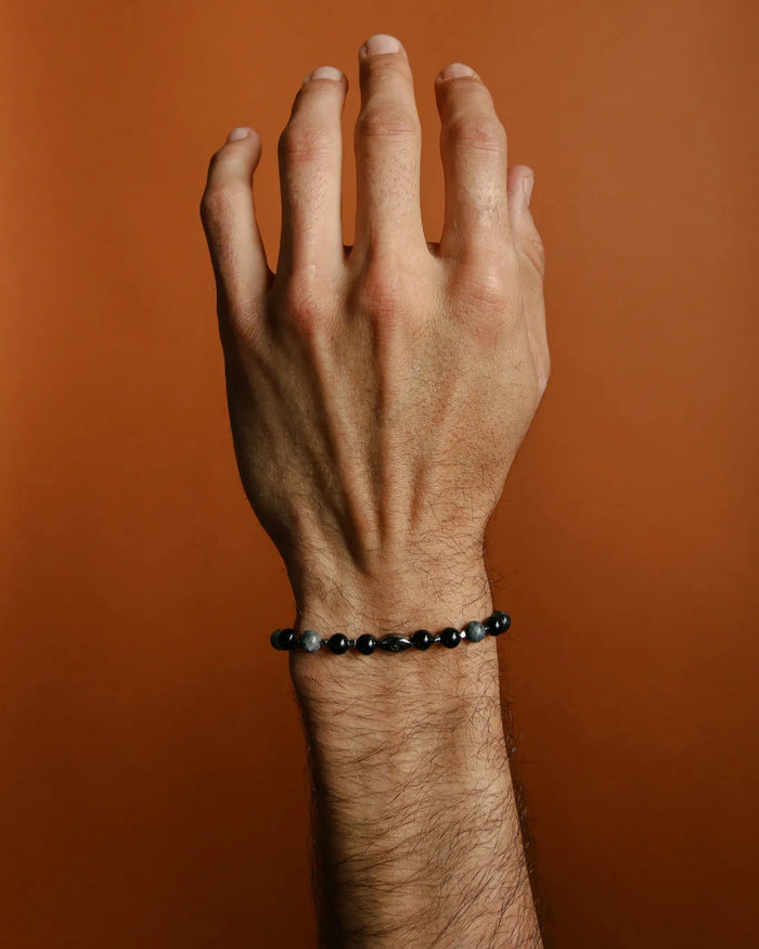 A close-up shot of a hand wearing a single David Bracelet in Black Rhodium, showcasing the bold matte black finish and black CZ diamond evil eye charm.
