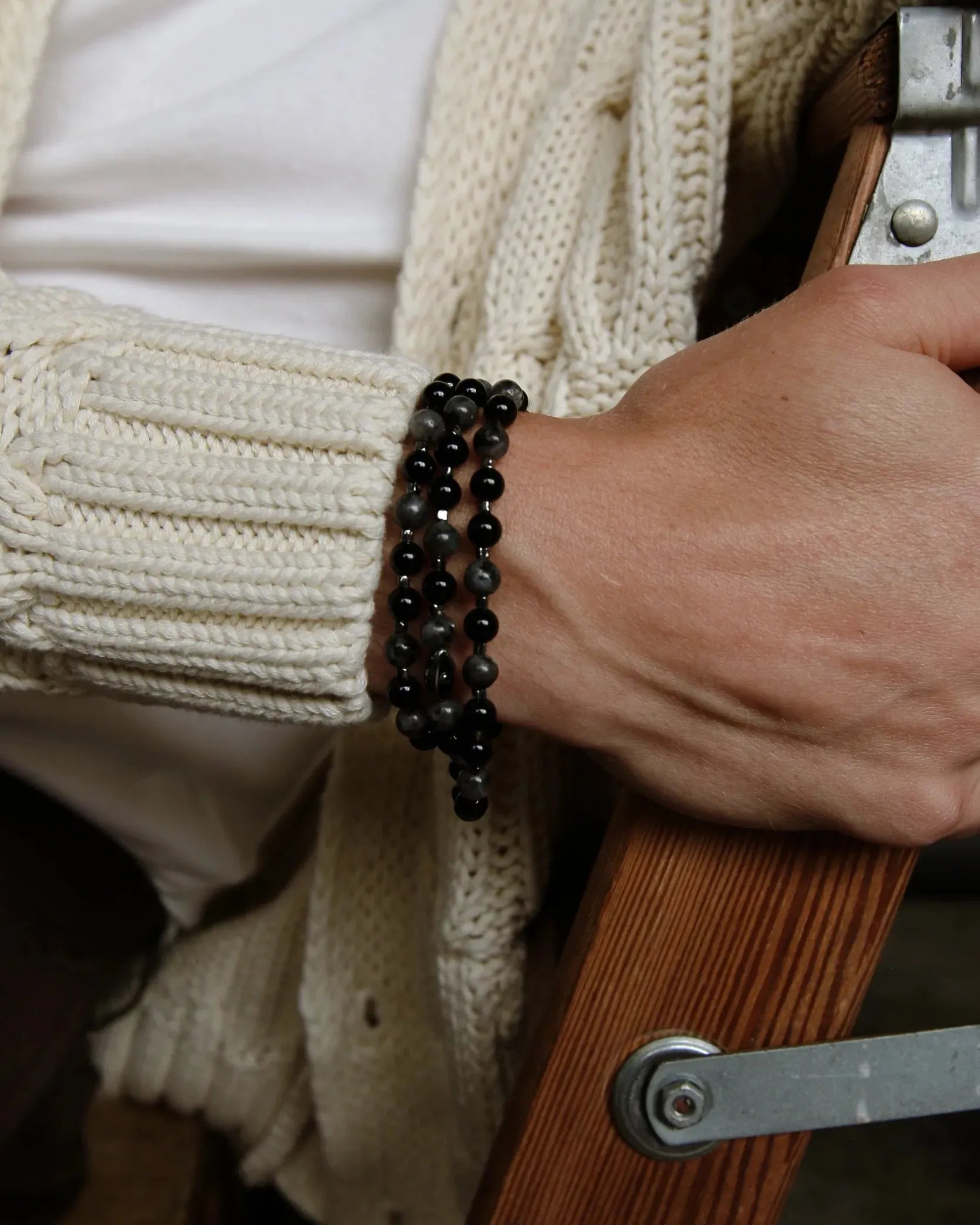 A man wearing the David Wrap in Black Rhodium as a bracelet, styled with a cream sweater and denim, showcasing the bracelet’s bold yet minimal look.