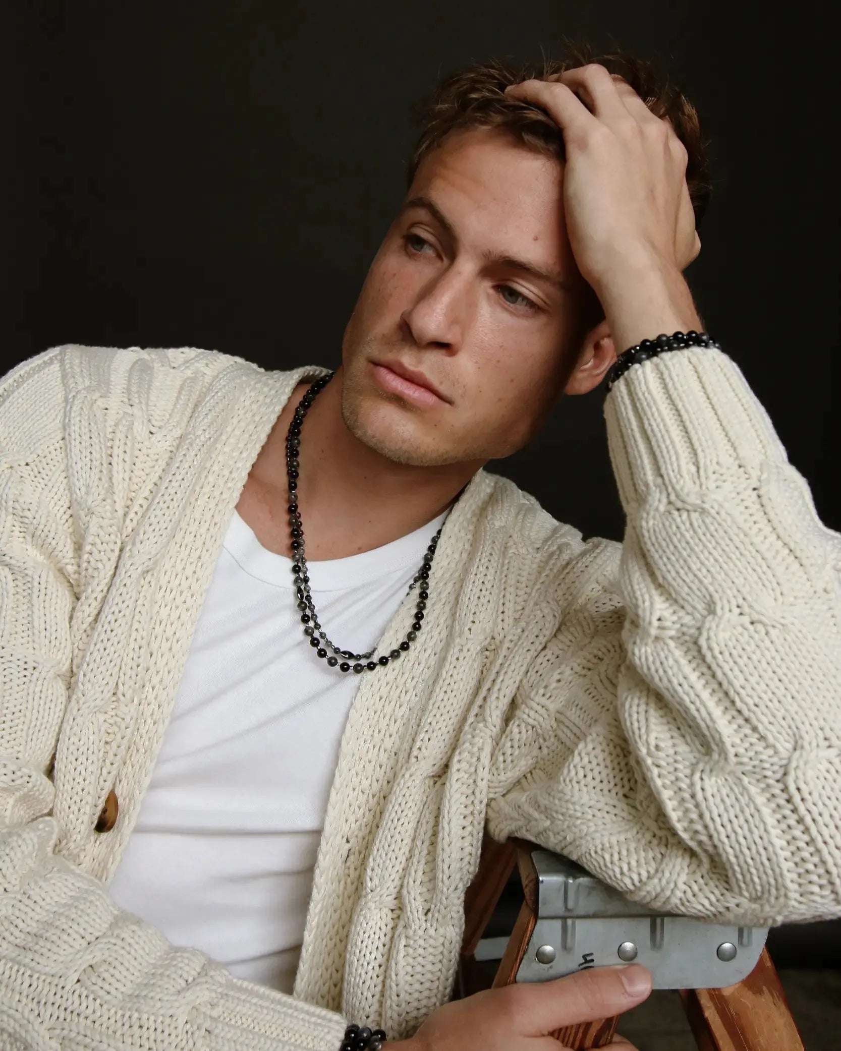 A man wearing the David Wrap in Black Rhodium as a necklace layered with a cozy, textured cardigan, highlighting the wrap’s versatility and dark, moody finish.
