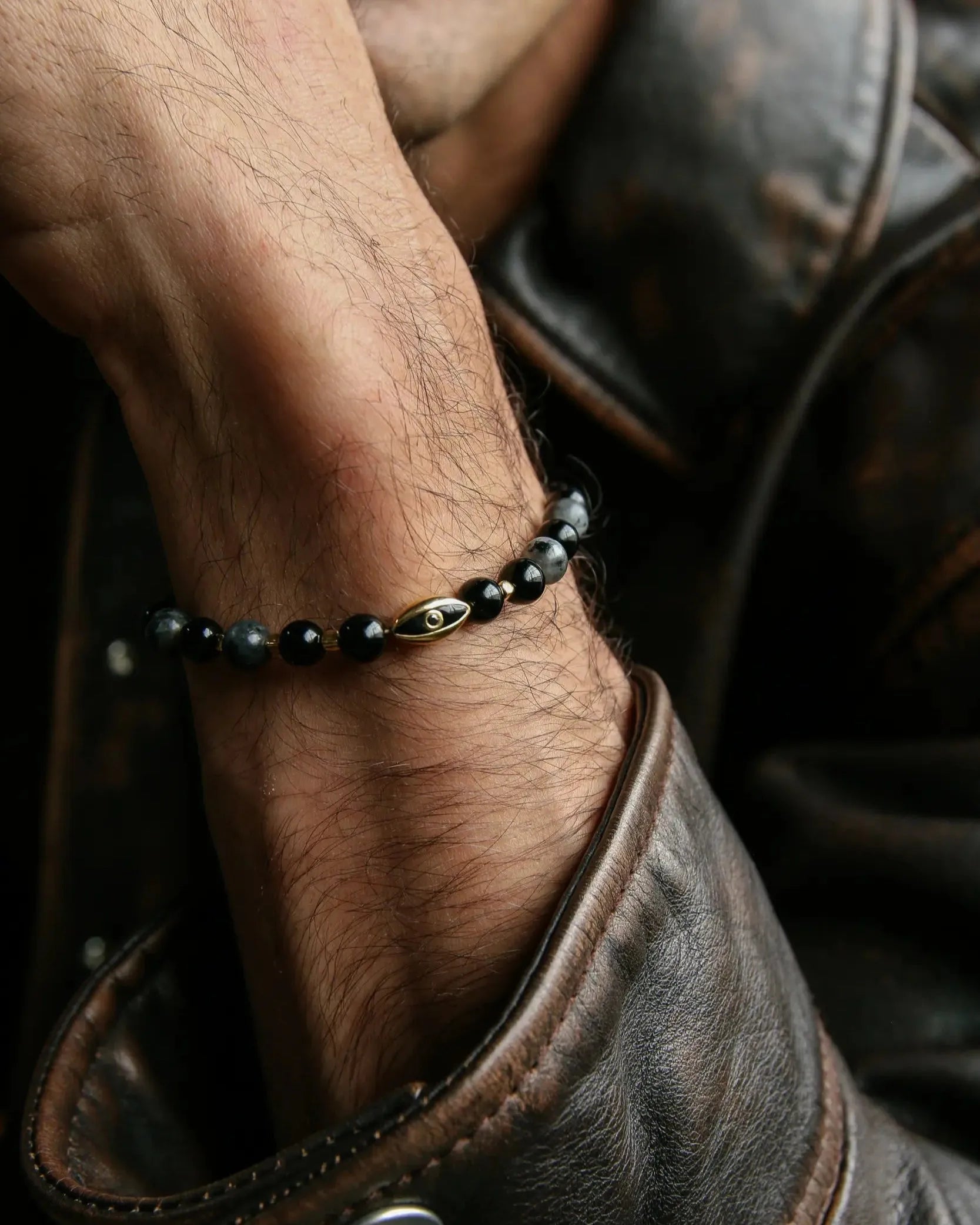 A man wearing the David Bracelet in 18K Gold, styled with a leather jacket, highlighting the bracelet’s refined gold plating and bold, dark beads.