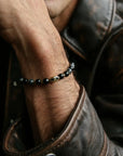 A man wearing the David Bracelet in 18K Gold, styled with a leather jacket, highlighting the bracelet’s refined gold plating and bold, dark beads.