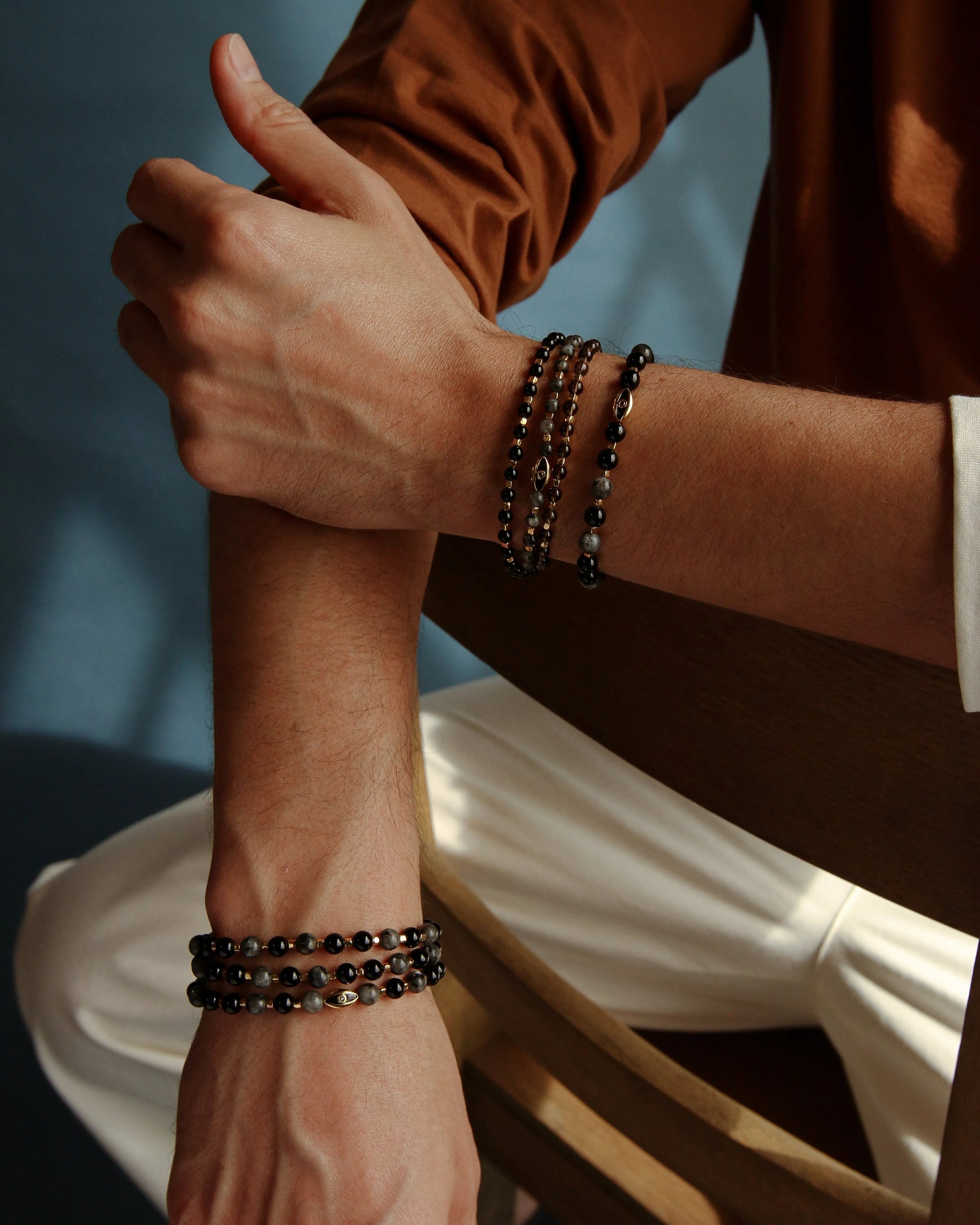 A man crossing his arms, styled with the David Bracelet in 18K Gold and the Ethan Wrap in 18K Gold, showcasing the contrast between the single bracelet and the wrap design for a bold, sophisticated look.