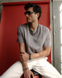 A man seated against a red backdrop, wearing the Ethan Wrap in Silver as a bracelet, styled casually with a relaxed, minimalist look.