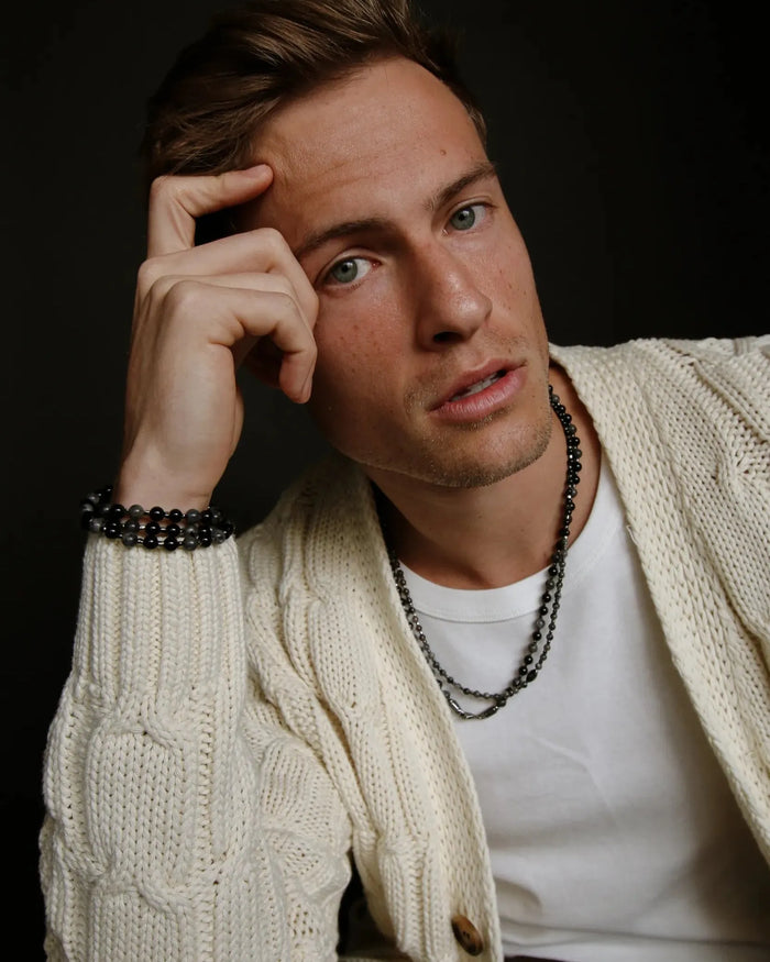 A man wearing the Ethan Wrap in Silver as a necklace, styled over a cream cardigan and white tee, emphasizing the wrap’s subtle, versatile design.