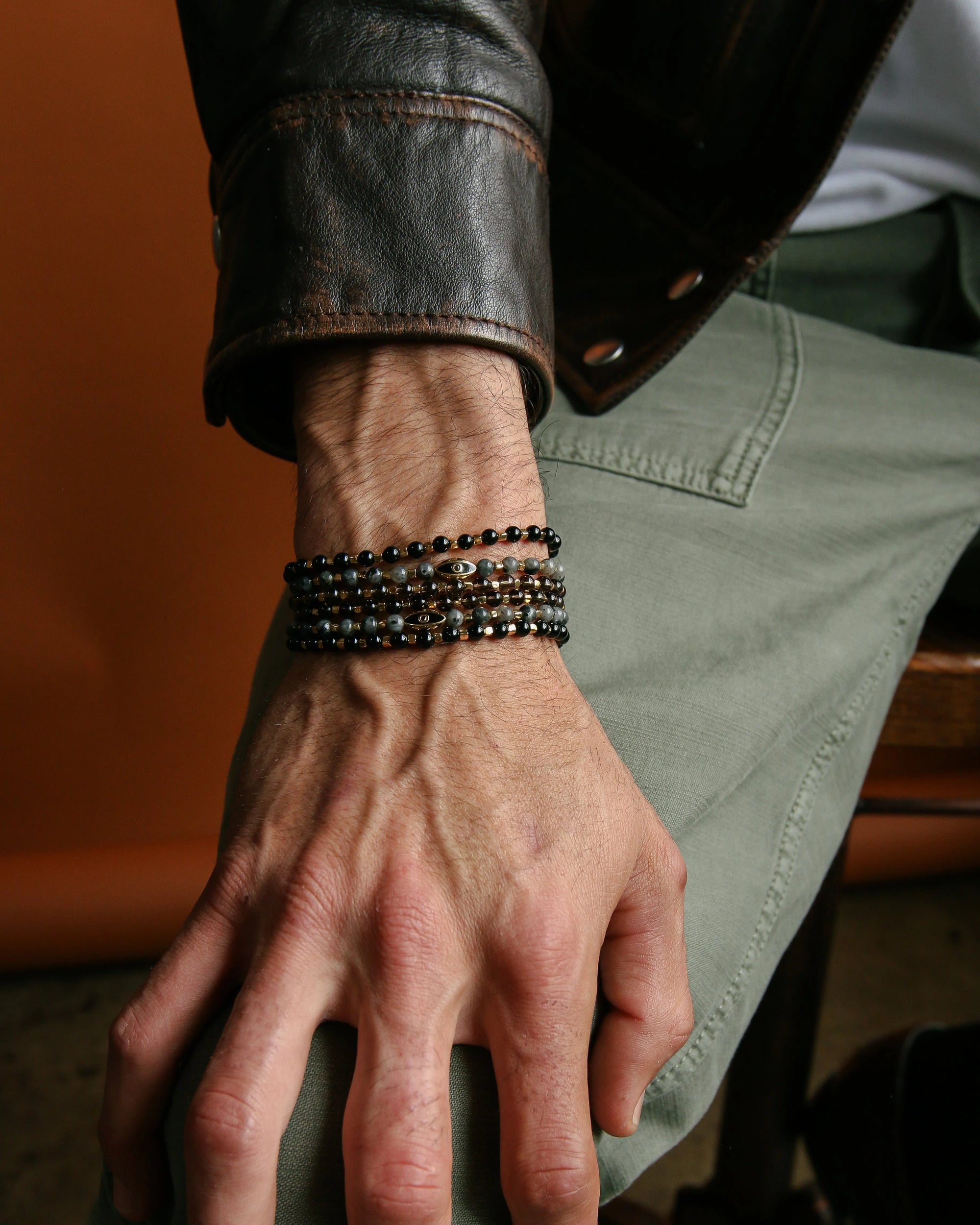 A close-up of a man’s wrist wearing the Ethan Wrap in 18K Gold as a bracelet, styled with a leather jacket for a bold, elevated look.