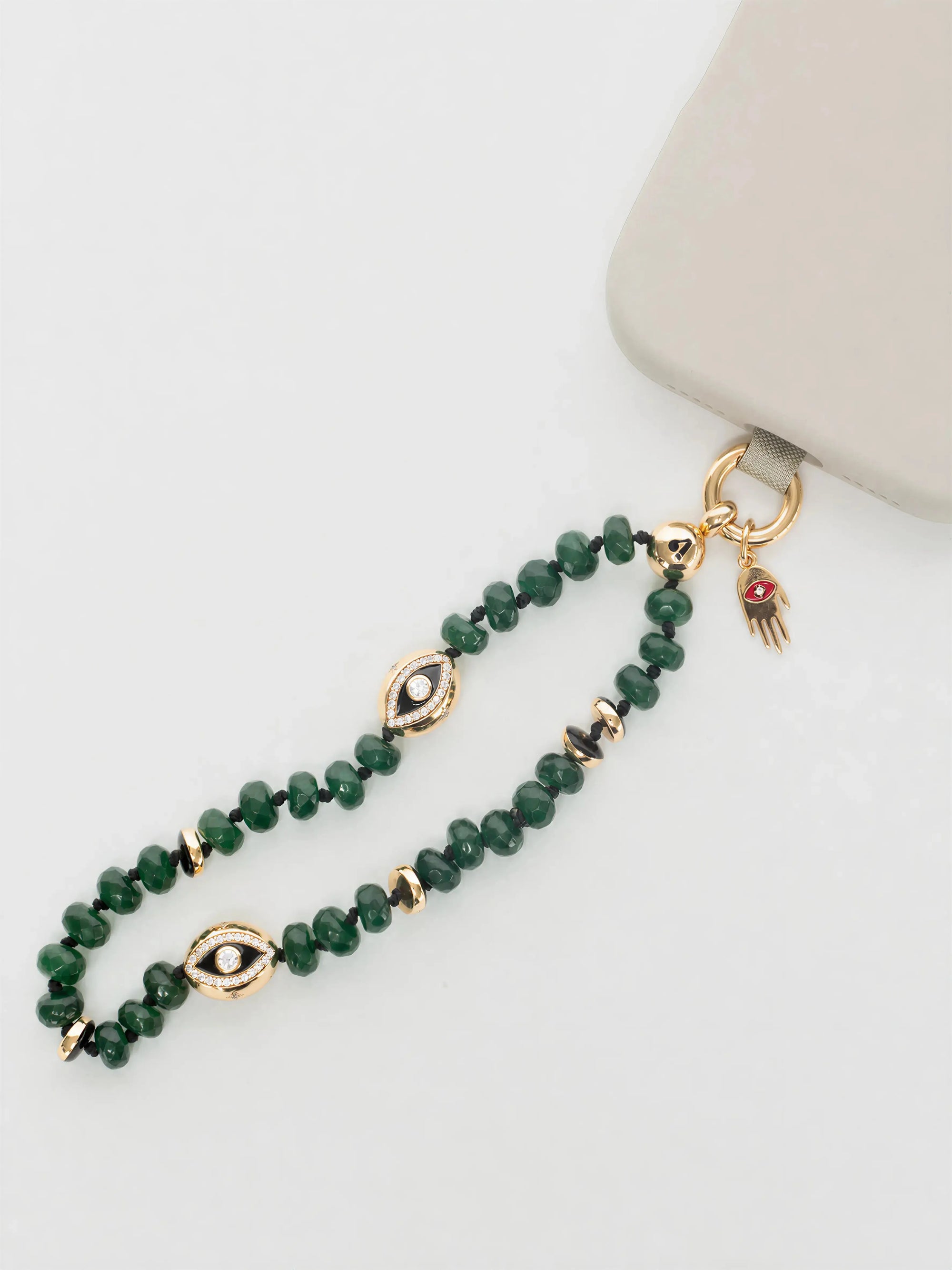 MyAleph Flat Hamsa evil eye charm styled with emerald phone charm strap, gold protective hand pendant with red enamel eye