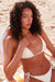 Woman in a white bikini sitting on a beach chair wear the MyAleph Mayra body chain in gold 