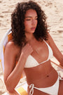 Woman in a white bikini sitting on a beach chair wear the MyAleph Mayra body chain in gold 