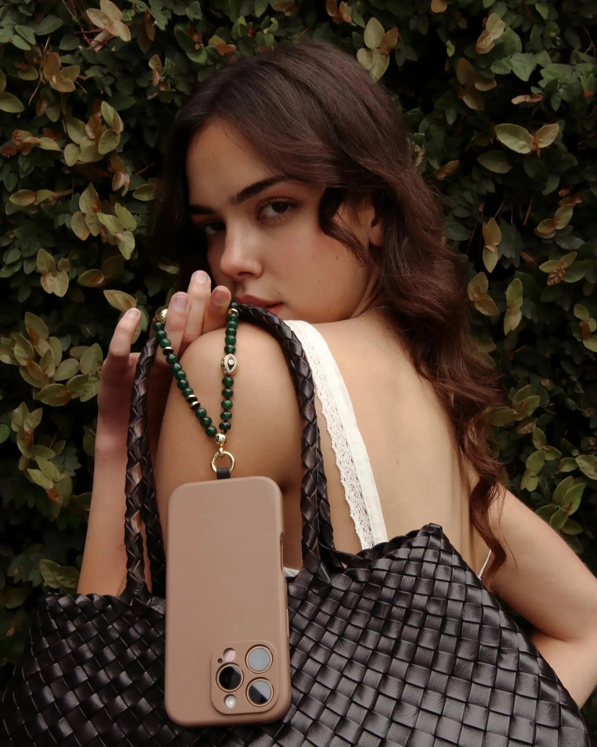 Model with soft curls holding her phone accessorized with the Leah Double Knot Wristlet in Emerald quartz.