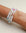 A set of three Leah white bracelets worn on the wrist, featuring milky white beads with colorful accents of pink, blue, and gold, highlighted by a central eye charm.