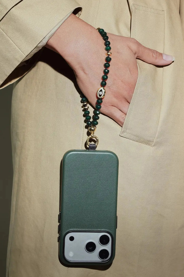 Phone case with a Emerald beaded strap held by a person wearing a beige coat.