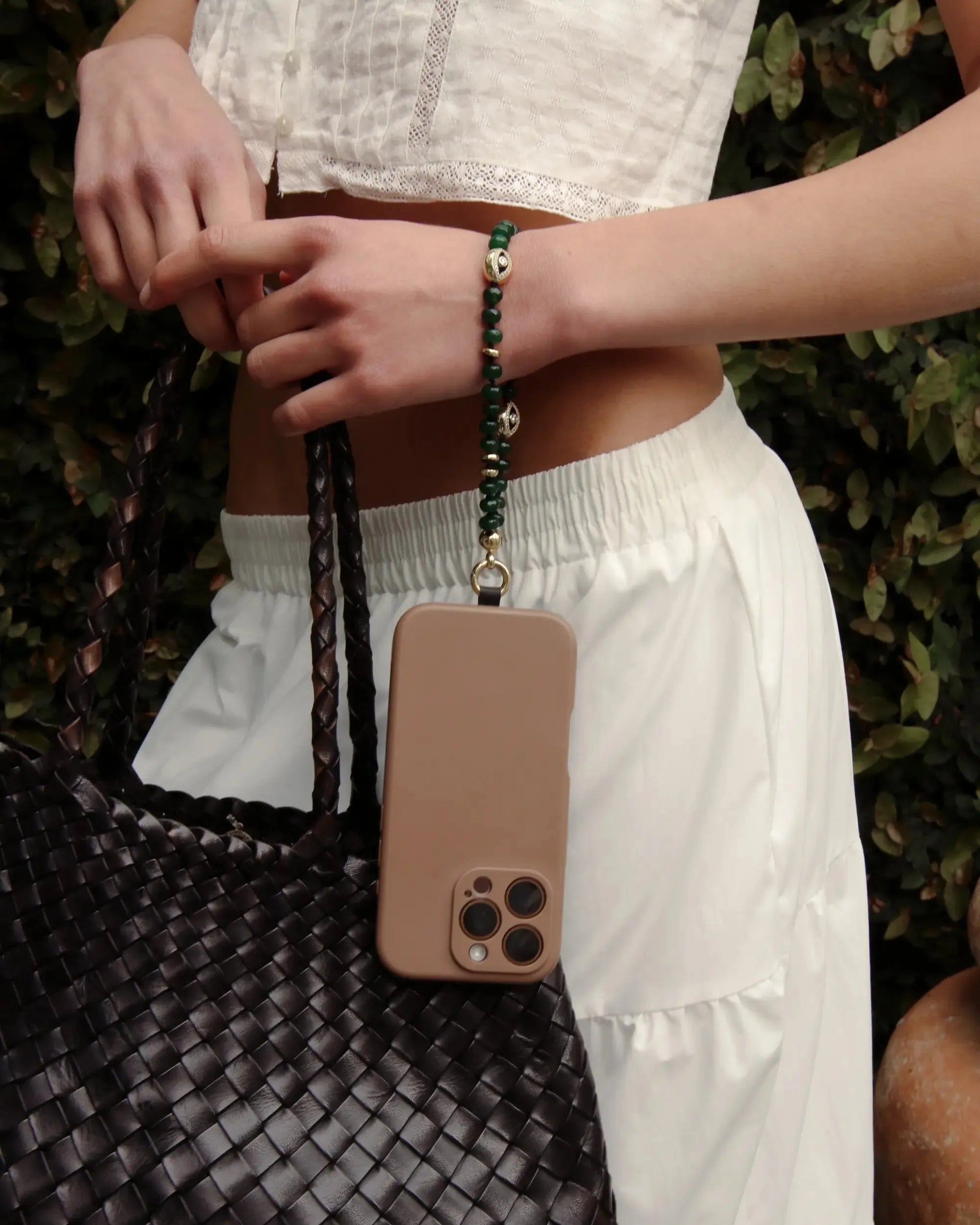 Close-up of the Leah Phone Charm in Emerald attached to a phone, styled on model wearing neutral tones.