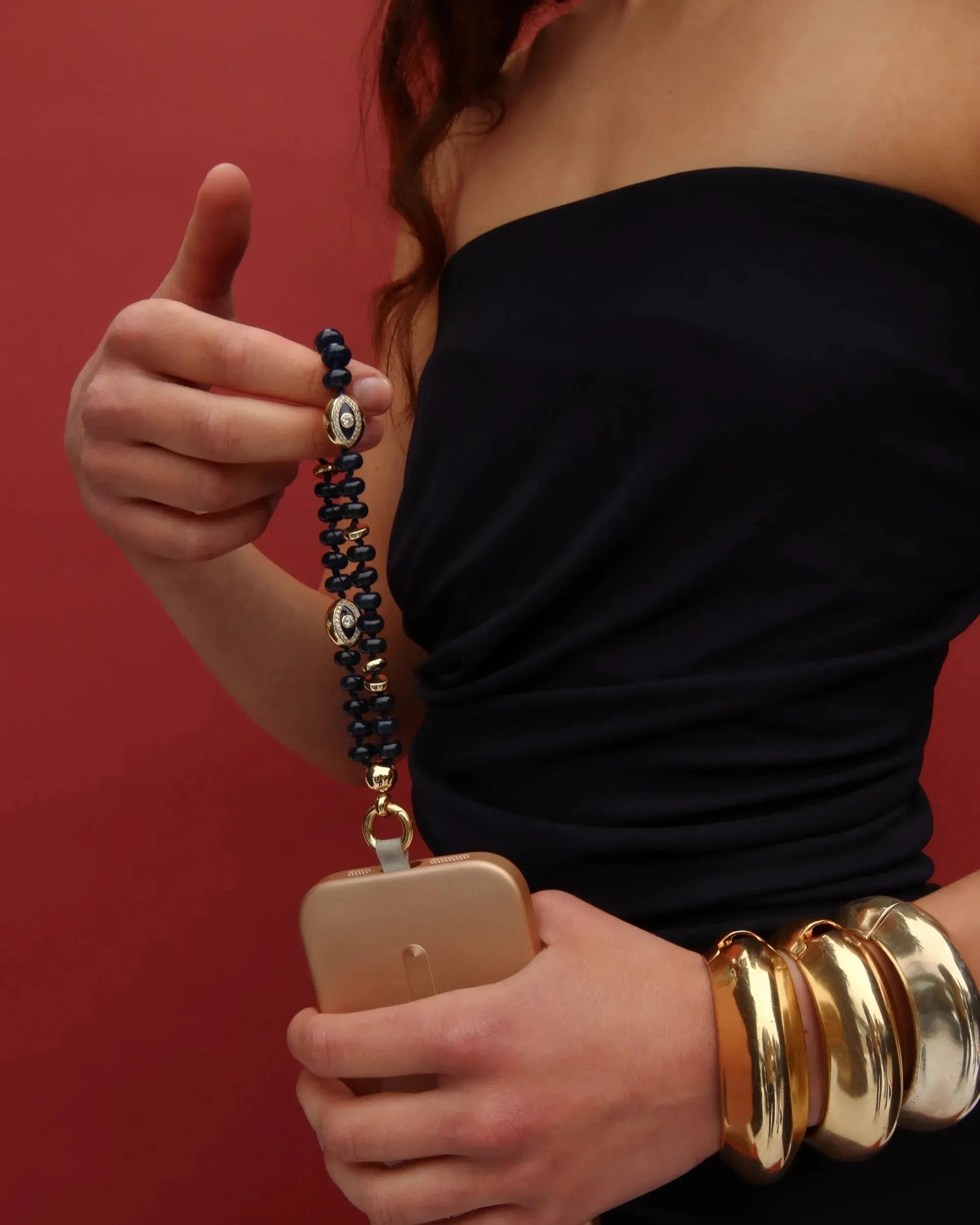Model wearing a black outfit holding the Leah Phone Charm in Sapphire quartz with stacked gold bangles.