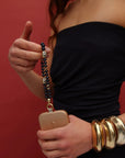 Model wearing a black outfit holding the Leah Phone Charm in Sapphire quartz with stacked gold bangles.