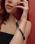 Close-up of model talking on the phone accessorized with the Leah Phone Charm in Sapphire against a red backdrop.