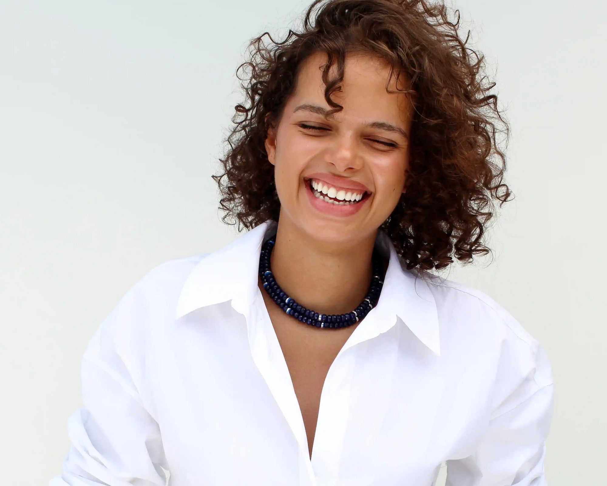 Model wearing the Lilou necklace in sapphire quartz with deep blue gemstone beads and gold plated hardware, styled against a clean light background.