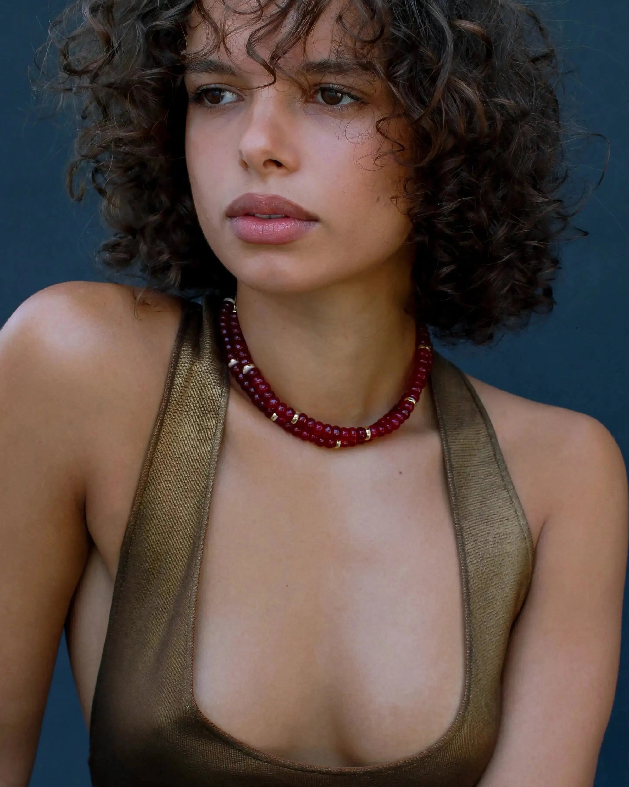 Model wearing the Lilou necklace in ruby quartz, showcasing the vibrant red beads and gold accents against the skin for a bold, statement look.