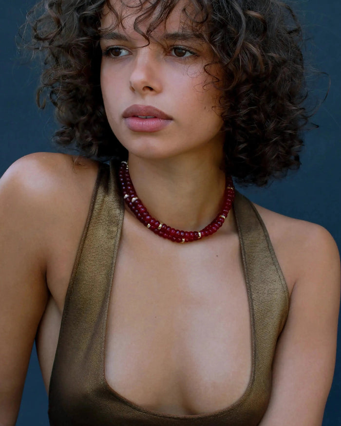 Model wearing the Lilou necklace in ruby quartz, showcasing the vibrant red beads and gold accents against the skin for a bold, statement look.