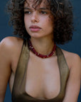 Model wearing the Lilou necklace in ruby quartz, showcasing the vibrant red beads and gold accents against the skin for a bold, statement look.