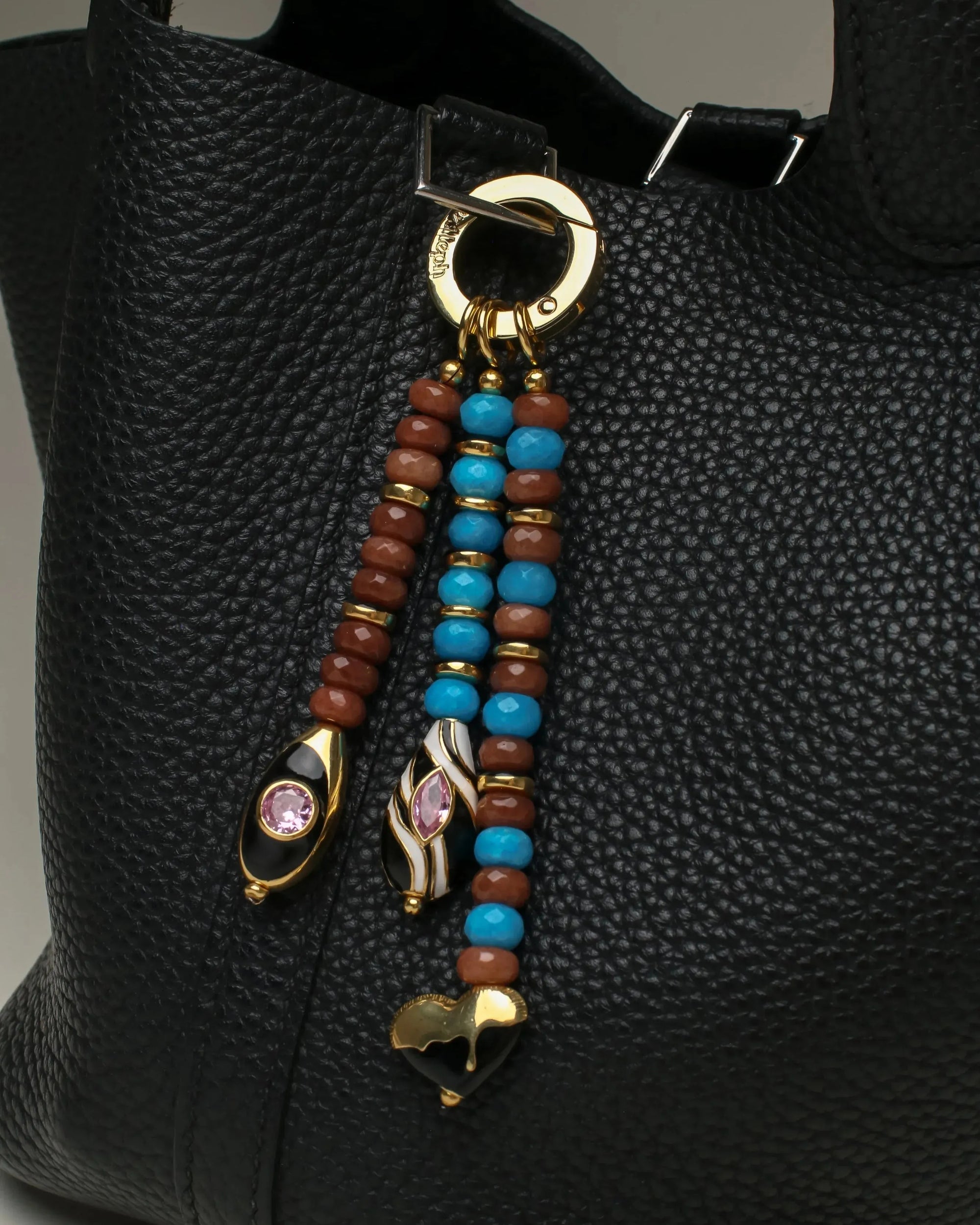The Liora Bag Charm in Azure &amp; Espresso attached to a black leather bag, adding an elegant and colorful accent.