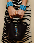 Close-up of the Liora Bag Charm in Azure & Espresso, featuring a striking combination of blue and brown quartz beads accented with gold details, attached to a black leather bag. The charm adds a playful yet elegant touch to the bold zebra-patterned outfit.