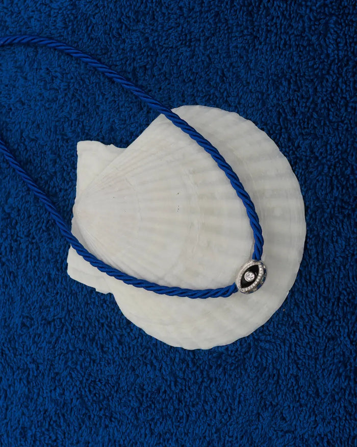 MyAleph Luna Cord Necklace in Azur with cobalt blue cord and silver evil eye pendant styled on seashell and blue textured background