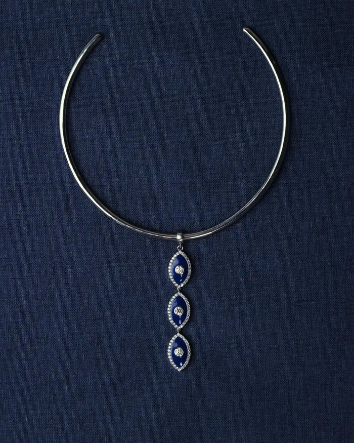 Silver choker necklace with blue evil eye pendant on a dark blue fabric background