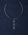 Silver choker necklace with blue evil eye pendant on a dark blue fabric background