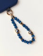 Mini Aura phone charm with blue apatite quartz beads and gold dipped evil eye talismans attached to a navy phone case on a white background.