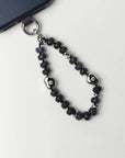 Mini Aura phone charm with smoky quartz beads and premium dipped silver evil eye talismans attached to black phone case on white background.