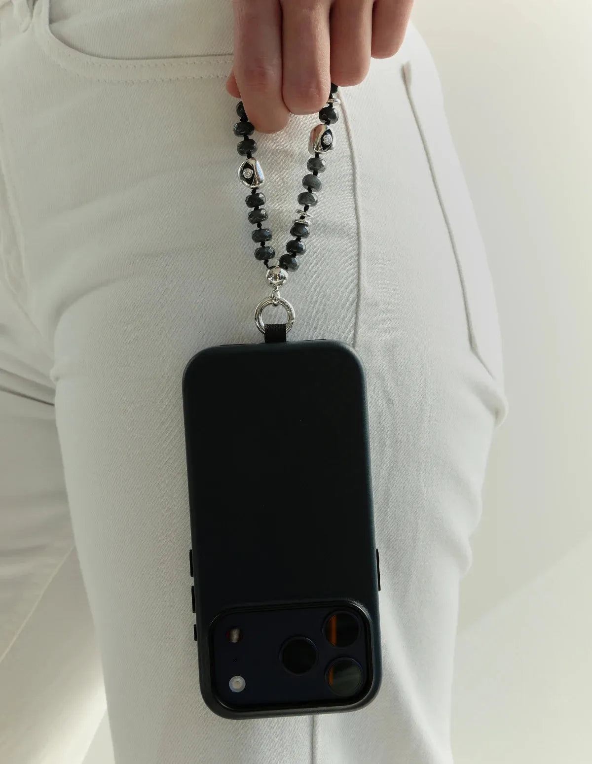 Model holding black phone with Mini Aura smoky quartz phone charm featuring silver dipped evil eye details.
