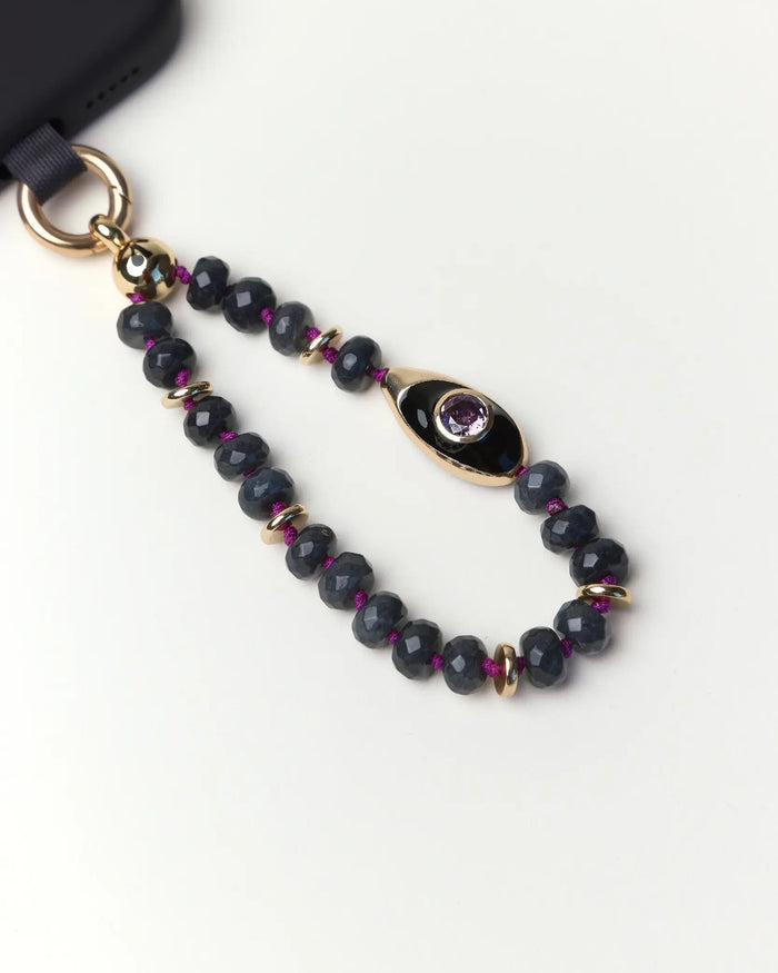 Close-up of Mini AYA phone charm featuring smoky quartz gemstone beads, gold accents, black evil eye charm, and amethyst CZ stone.