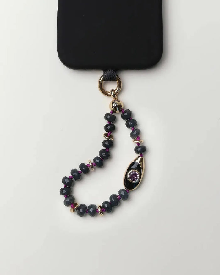 Mini Aya phone charm with smoky quartz gemstone beads, gold accents, evil eye charm, and amethyst CZ stone attached to a black phone case.