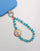 Aqua Quartz Mini India phone charm with Evil Eye Sun Charm and 18K Gold-Plated Hardware – Flat Lay on White Background with Blue Phone Case
