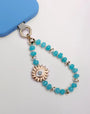 Aqua Quartz Mini India phone charm with Evil Eye Sun Charm and 14k Gold-Plated Hardware – Flat Lay on White Background with Blue Phone Case