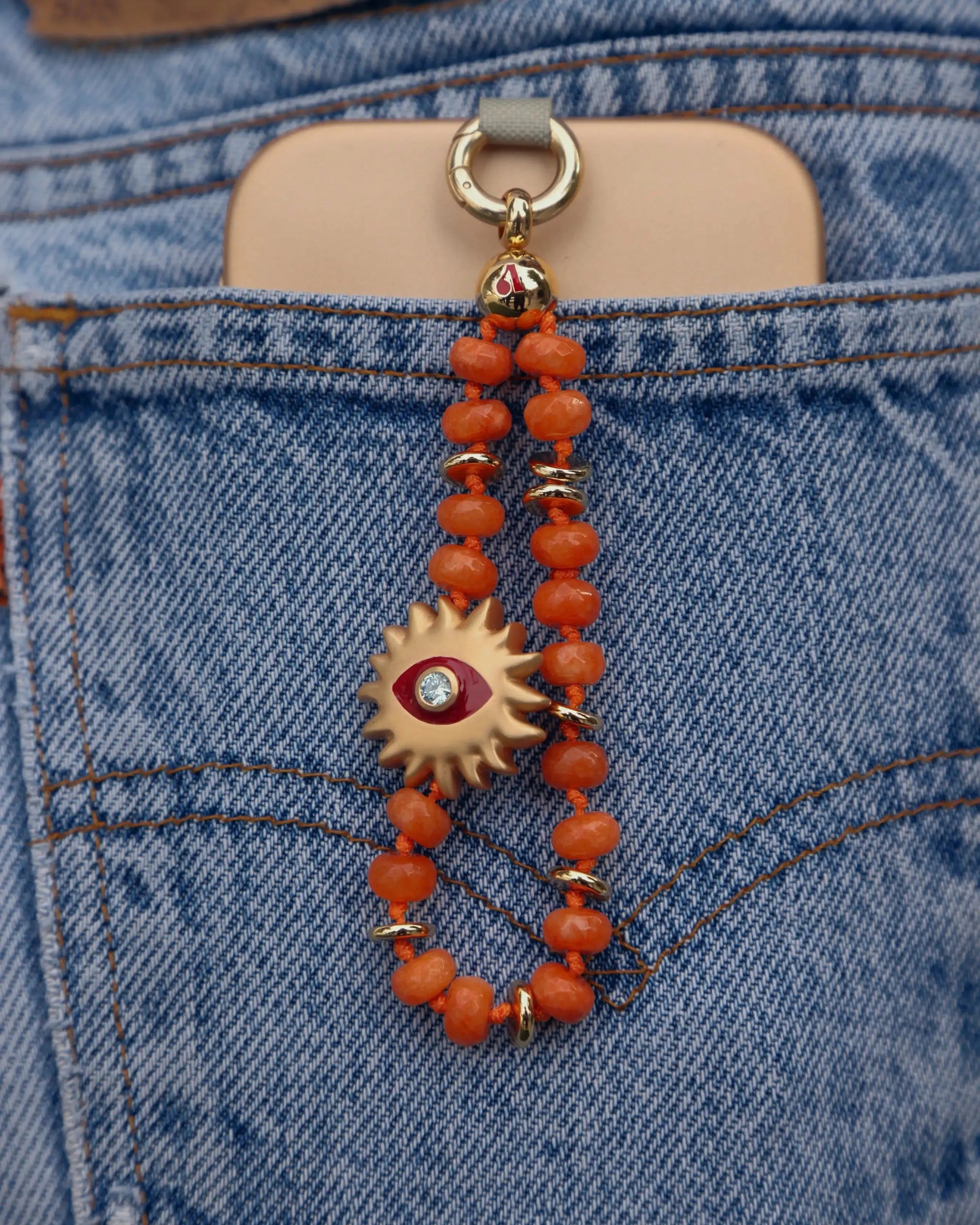 Clementine Quartz Mini India Phone Charm with Sun Evil Eye Charm clipped to phone in back pocket of blue denim jeans