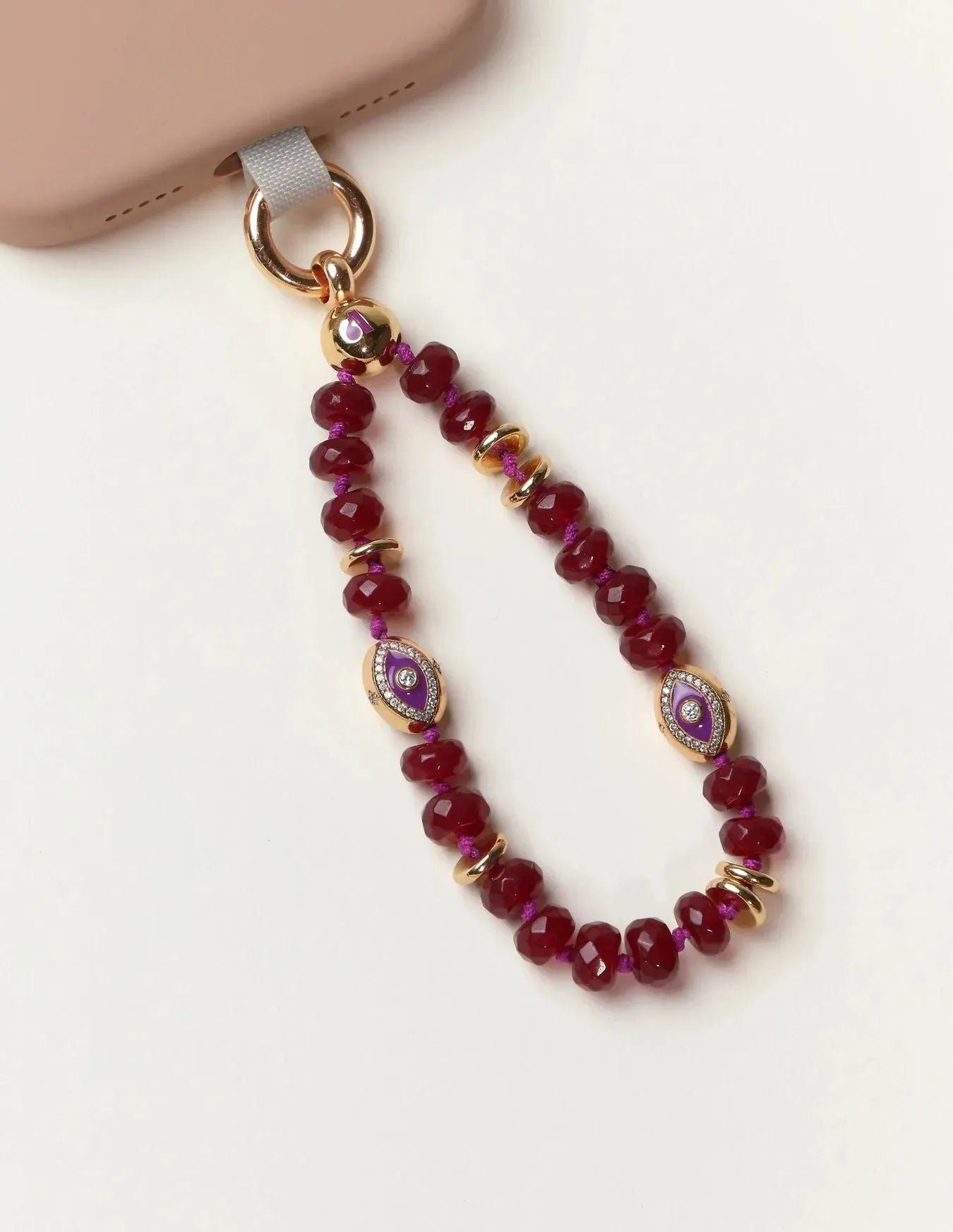 Mini Leah Ruby Quartz Phone Charm with evil eye beads and 14k gold accents attached to phone case.