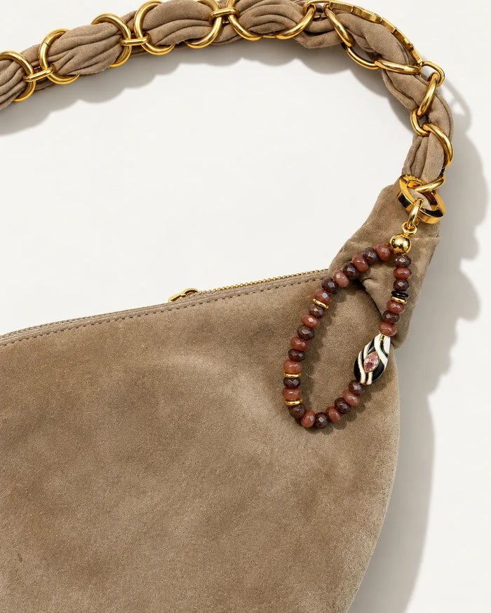 Espresso Mini Minou Bag Charm hanging from a taupe suede handbag with a gold chain strap, showcasing brown quartz beads and gold accents.
