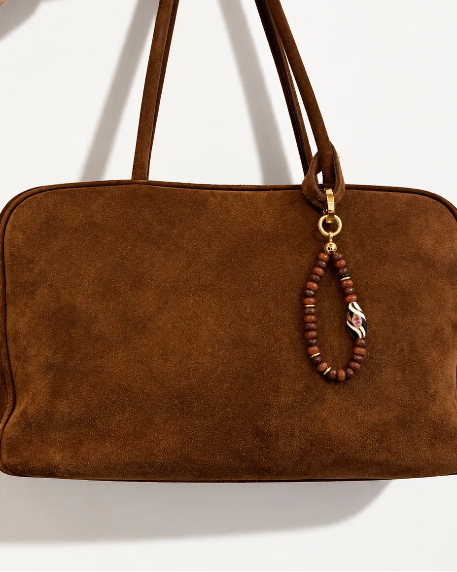 Mini Minou Bag Charm in Espresso quartz styled on a chocolate brown suede shoulder bag, featuring faceted quartz beads, gold spacers, and a zebra evil eye charm.