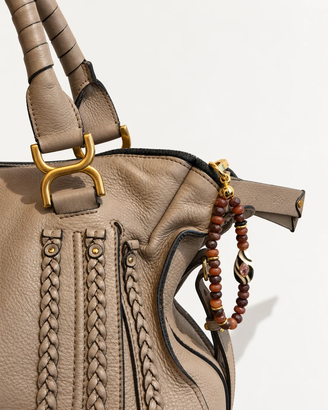 Mini Minou Espresso Bag Charm attached to a taupe braided leather handbag, featuring brown quartz beads, gold hardware, and a zebra evil eye detail.