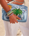 Model holding MyAleph Large Pampelonne Denim Pouch with embroidered sun and palm design, styled with Riviera Bracelets, and belly chain.