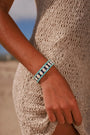 MyAleph Riviera Bracelet in Capri — navy and turquoise evil eye protective charm bracelet worn on wrist, styled with a cream knit summer dress on the beach.