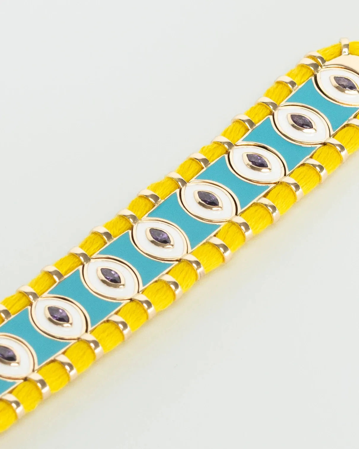 Close-up of MyAleph Riviera Bracelet with yellow cotton cord, turquoise enamel evil eye details, and adjustable clasp