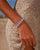 MyAleph Riviera Bracelet in Saint Tropez — emerald green and hot pink evil eye protective charm bracelet worn on wrist, styled with a cream knit summer dress on the beach.